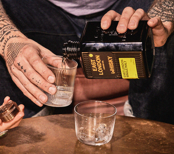 A man sitting holding a glass of whisky next to a bottle of East London Single Malt.